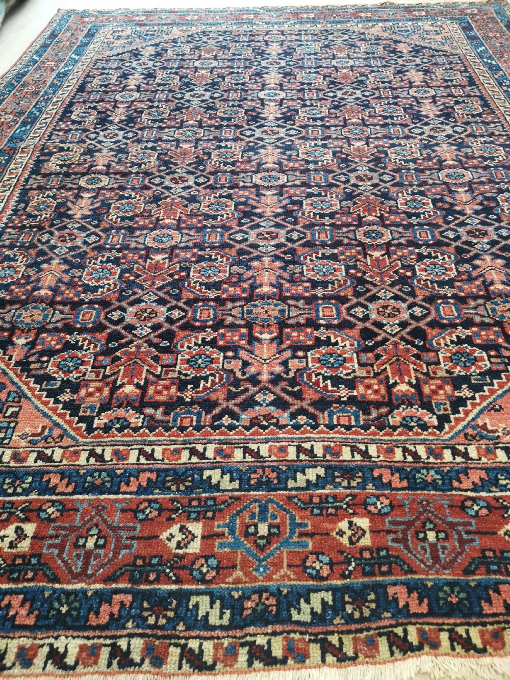 A hand-knotted antique Persian Hamadan wool rug featuring a navy blue field with geometric repeats framed by a terracotta spandrel and detailed multi-band border. View VI