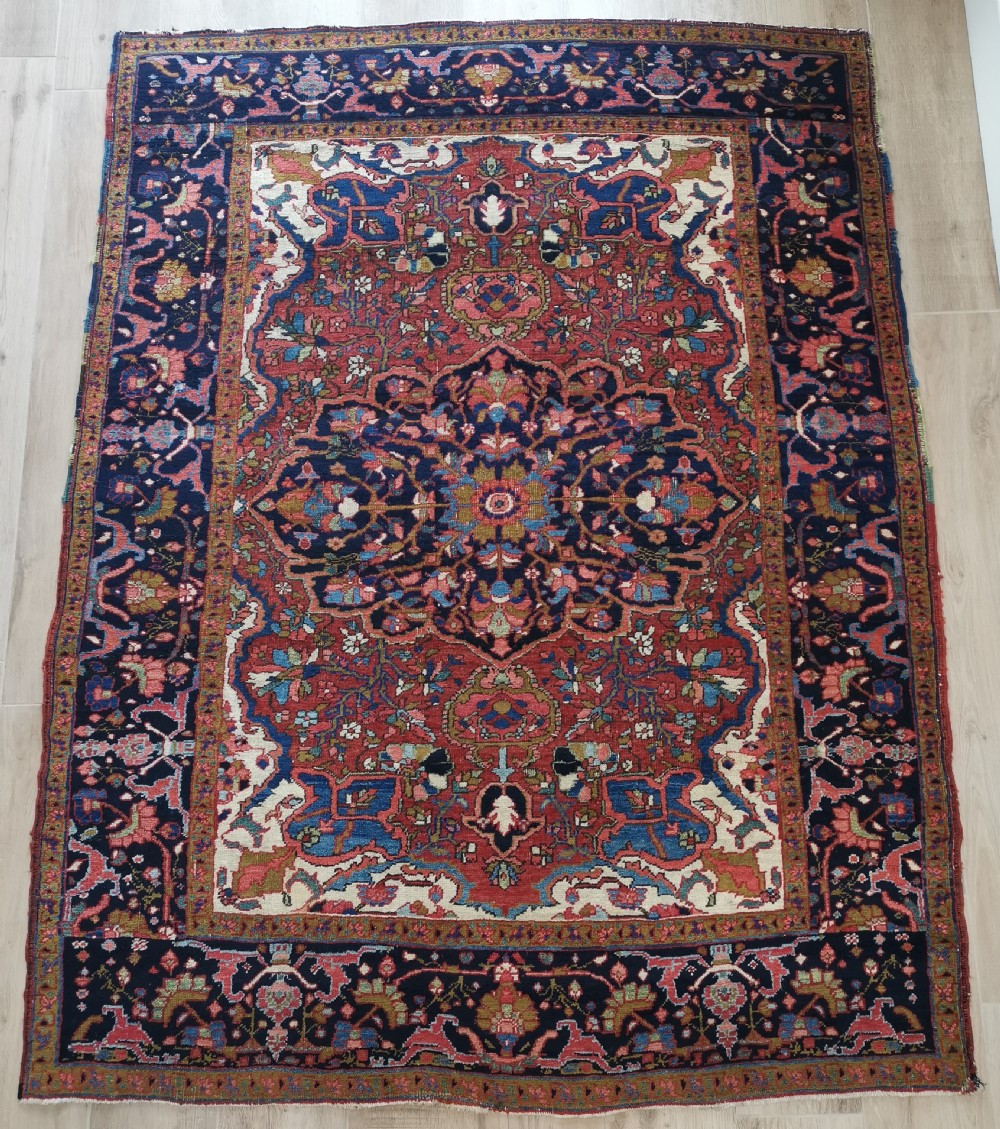 A rectangular hand-knotted Persian rug featuring a central geometric medallion surrounded by floral borders in red, navy blue, and cream.