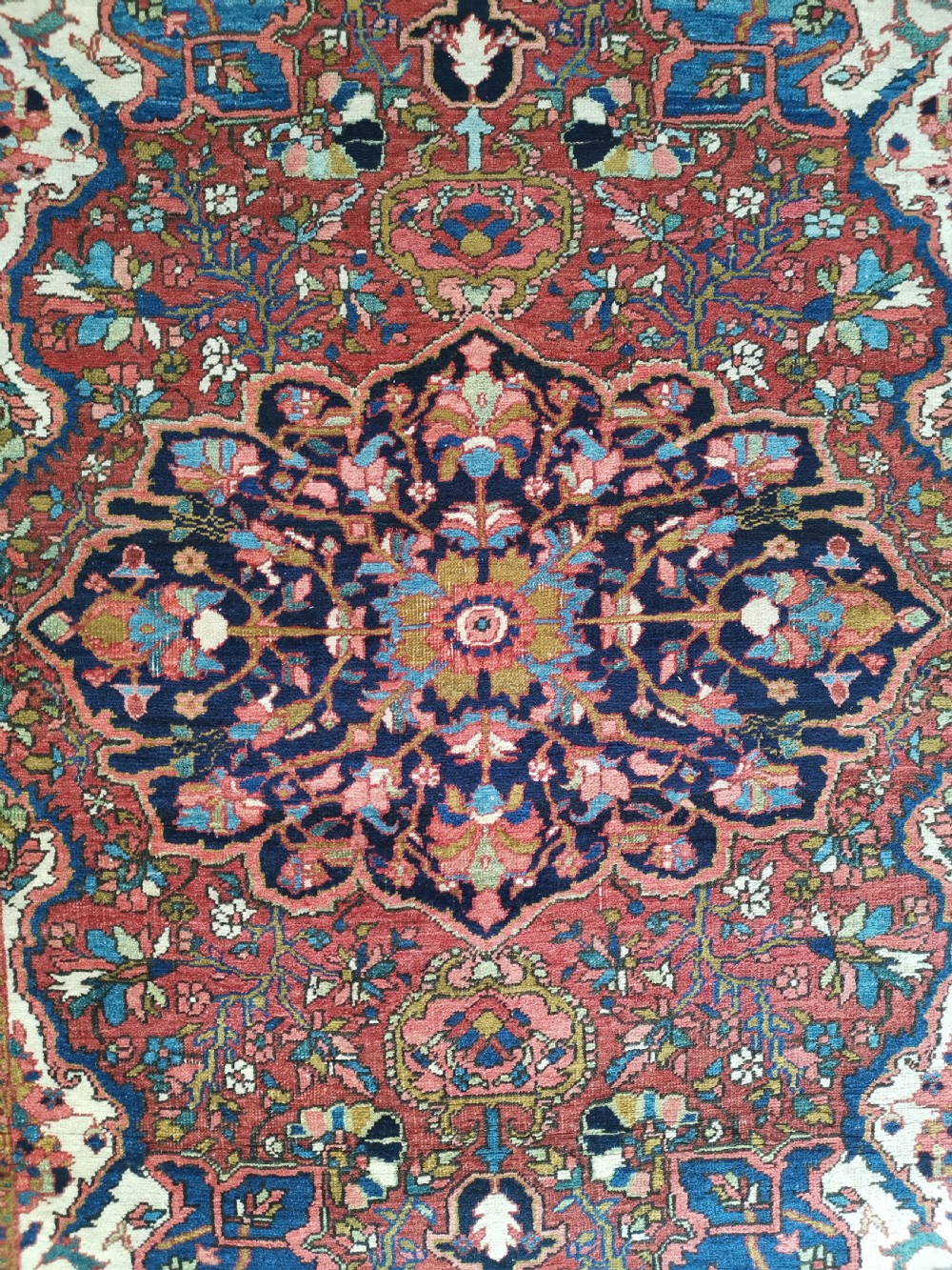 A rectangular hand-knotted Persian rug featuring a central geometric medallion surrounded by floral borders in red, navy blue, and cream. View II