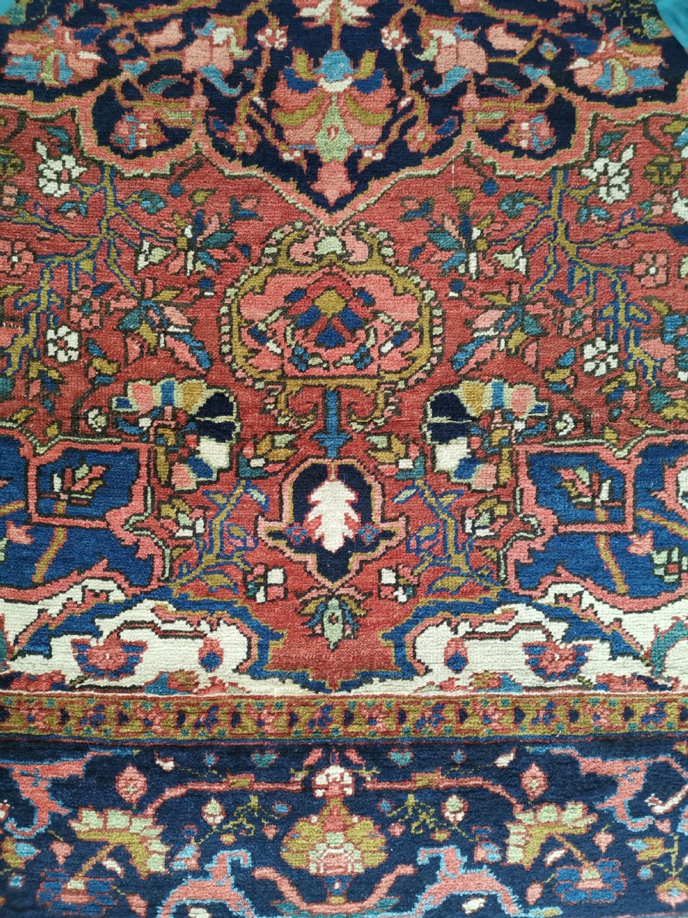 A rectangular hand-knotted Persian rug featuring a central geometric medallion surrounded by floral borders in red, navy blue, and cream. View III