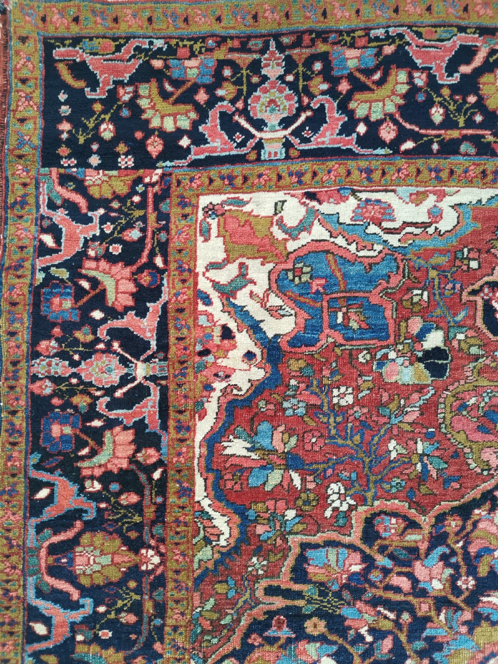 A rectangular hand-knotted Persian rug featuring a central geometric medallion surrounded by floral borders in red, navy blue, and cream. View IV