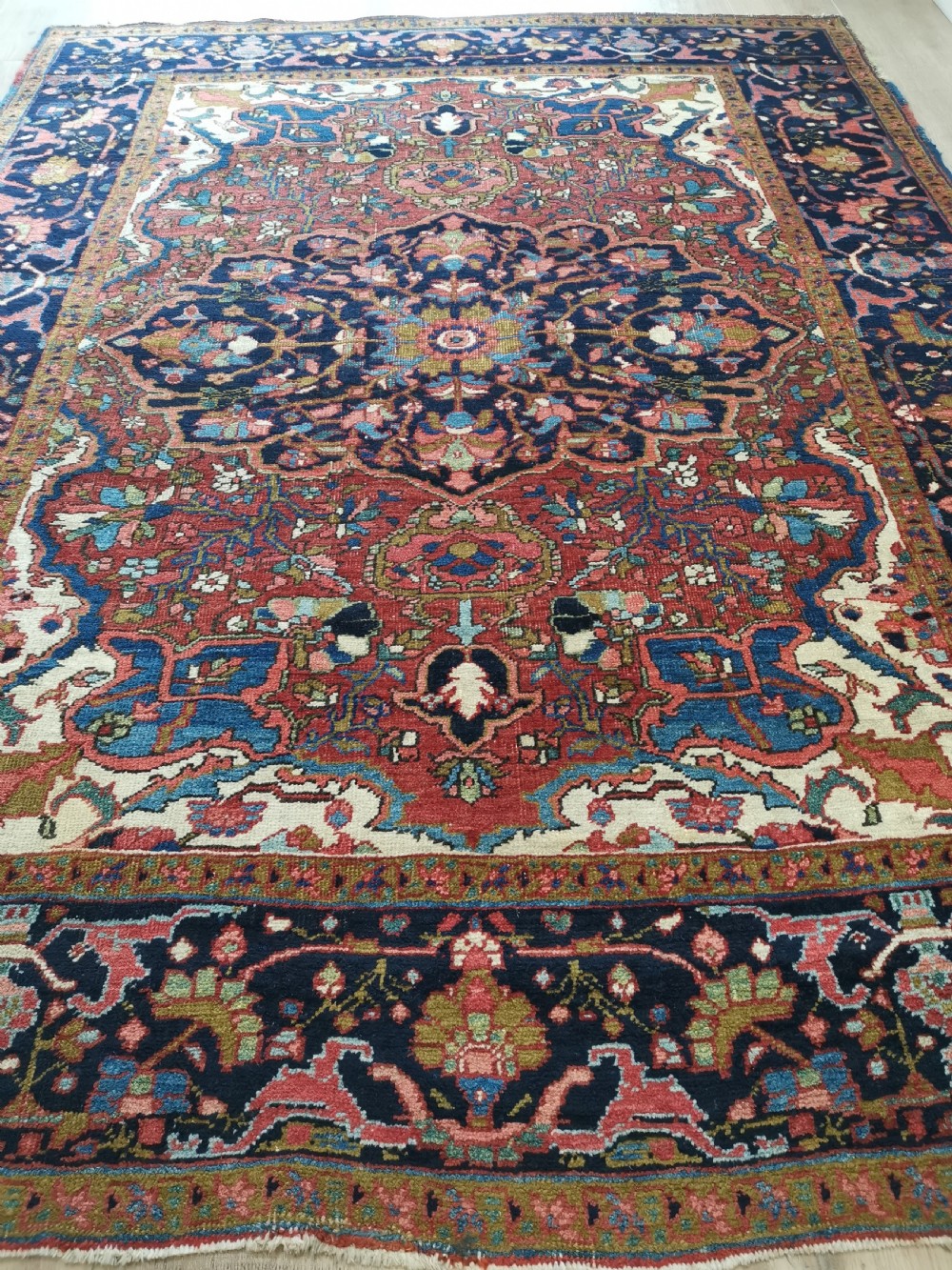 A rectangular hand-knotted Persian rug featuring a central geometric medallion surrounded by floral borders in red, navy blue, and cream. View V