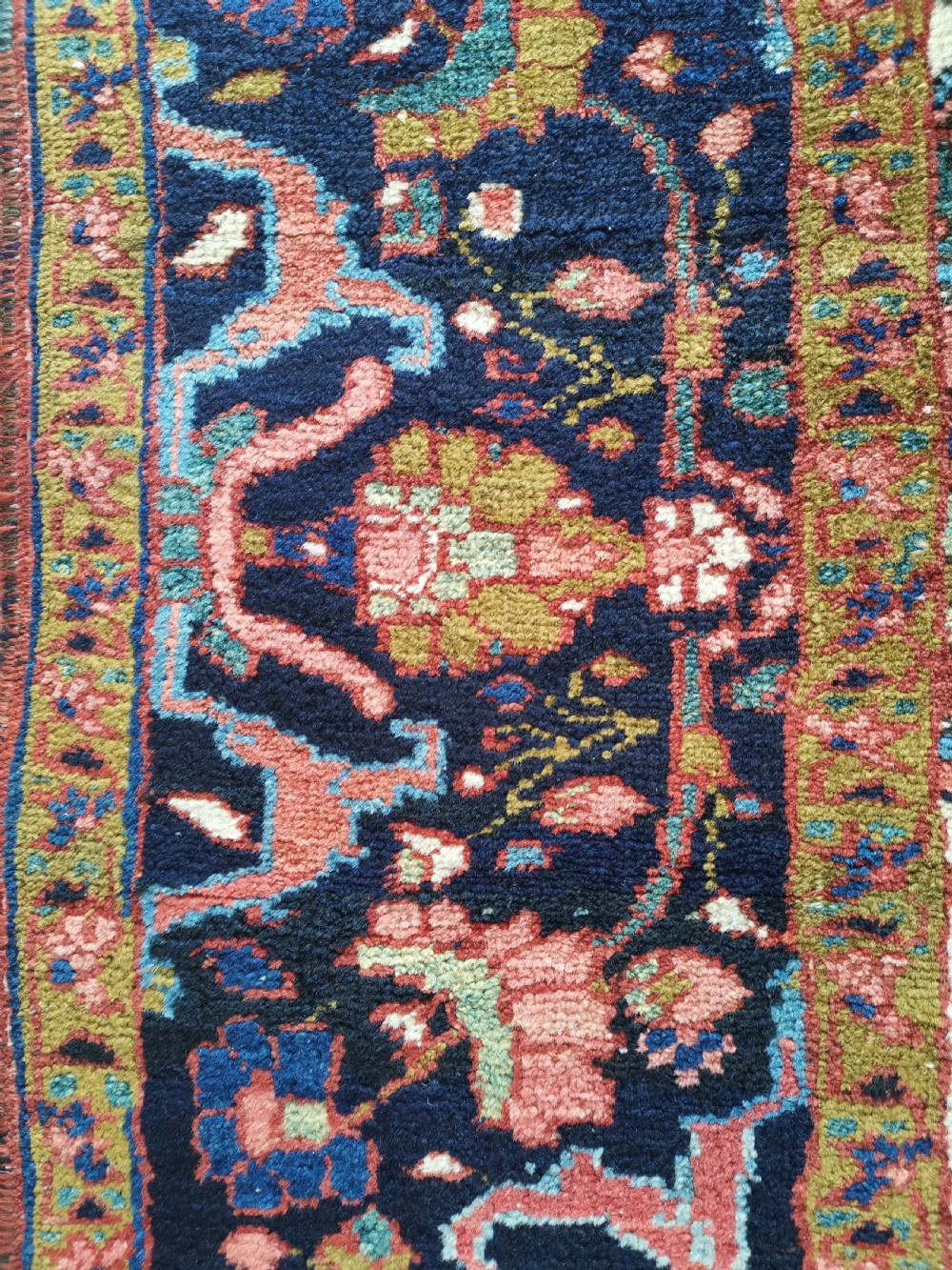 A rectangular hand-knotted Persian rug featuring a central geometric medallion surrounded by floral borders in red, navy blue, and cream. View VI