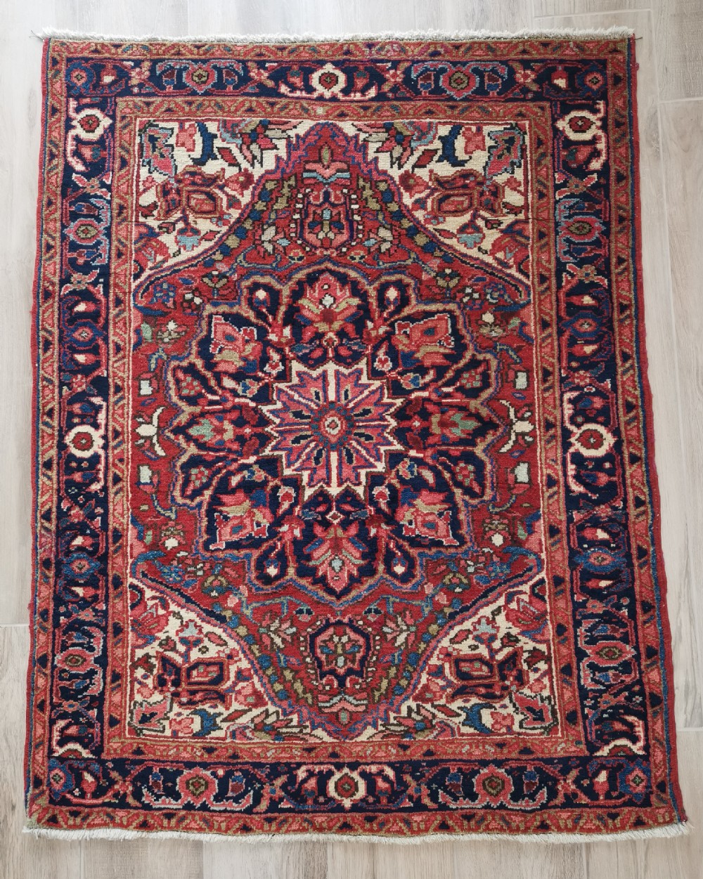 A hand-knotted wool Heriz area rug displaying a central star medallion in navy and cream against a brick red field with geometric borders.