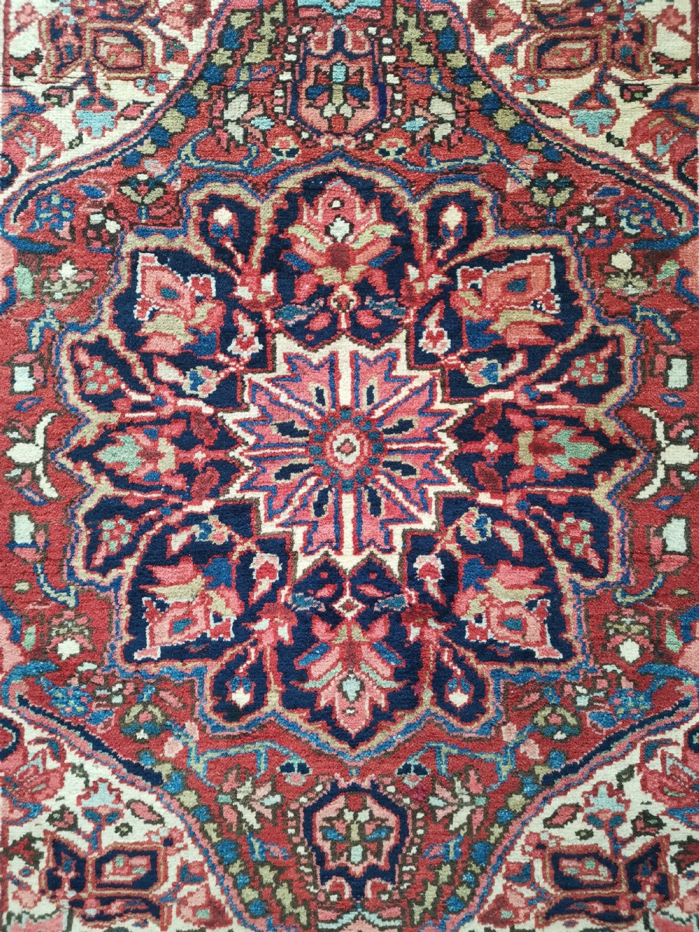 A hand-knotted wool Heriz area rug displaying a central star medallion in navy and cream against a brick red field with geometric borders. View II
