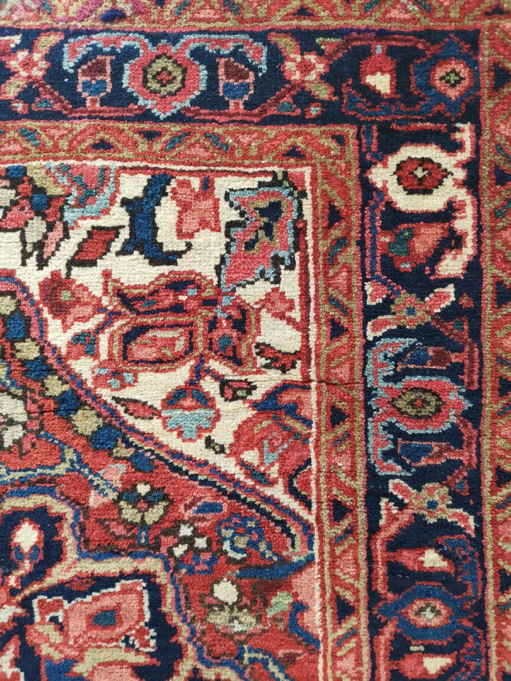 A hand-knotted wool Heriz area rug displaying a central star medallion in navy and cream against a brick red field with geometric borders. View III