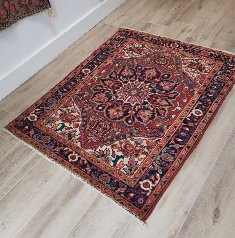 A hand-knotted wool Heriz area rug displaying a central star medallion in navy and cream against a brick red field with geometric borders. View IV
