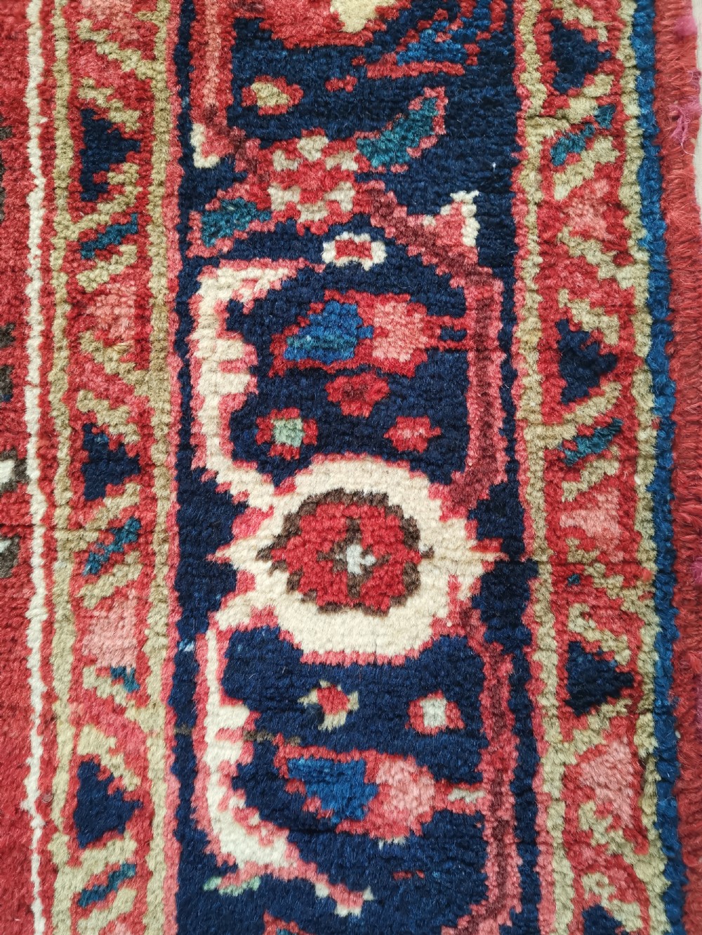 A hand-knotted wool Heriz area rug displaying a central star medallion in navy and cream against a brick red field with geometric borders. View V