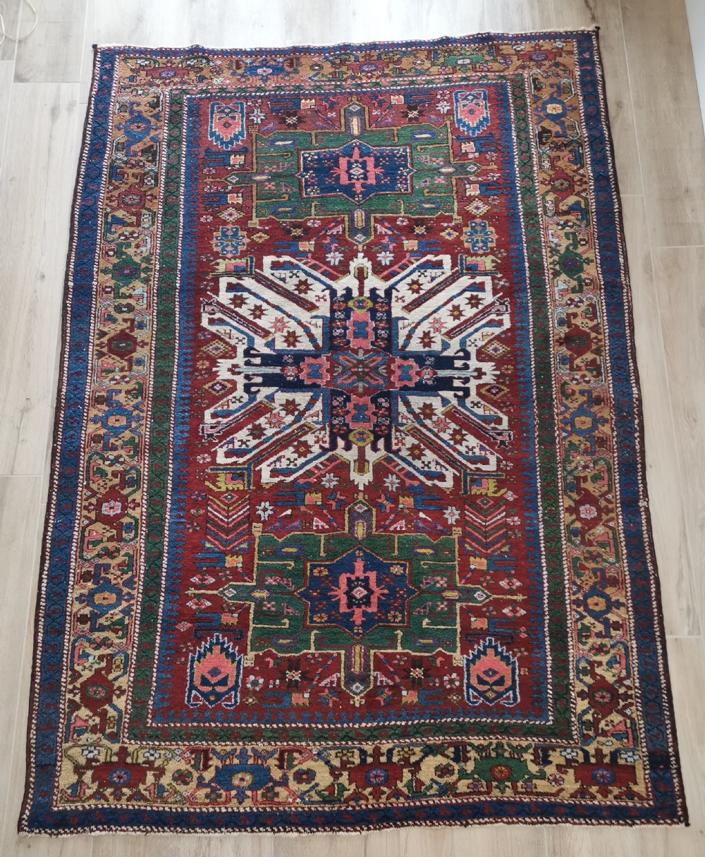 A hand-knotted antique Karaja wool rug featuring an ivory and navy geometric central medallion flanked by smaller star motifs on a deep red field with multi-coloured borders.