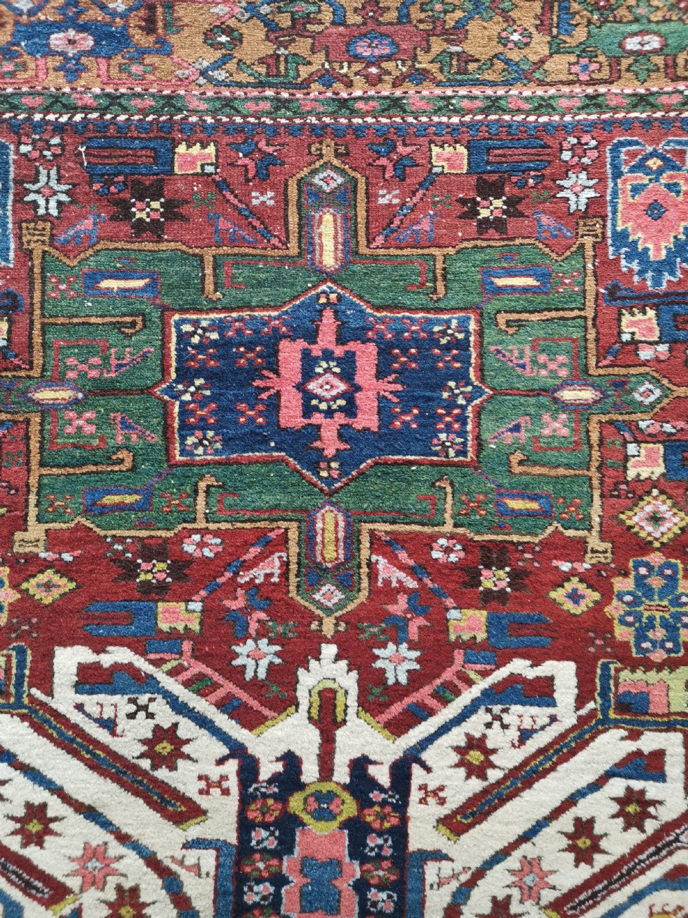 A hand-knotted antique Karaja wool rug featuring an ivory and navy geometric central medallion flanked by smaller star motifs on a deep red field with multi-coloured borders. View III