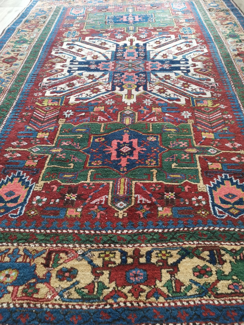 A hand-knotted antique Karaja wool rug featuring an ivory and navy geometric central medallion flanked by smaller star motifs on a deep red field with multi-coloured borders. View IV