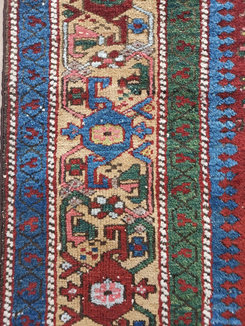 A hand-knotted antique Karaja wool rug featuring an ivory and navy geometric central medallion flanked by smaller star motifs on a deep red field with multi-coloured borders. View V