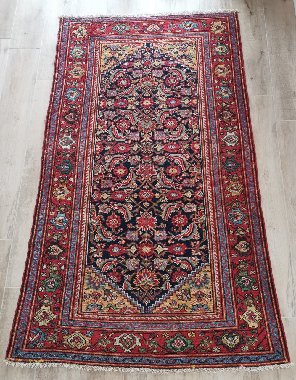 A rectangular hand-knotted antique Persian Fereghan wool rug featuring a dark navy central field with dense floral Herati patterns, framed by a red and blue multi-band border.