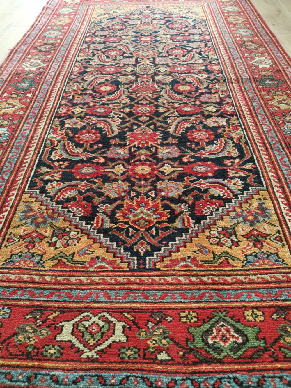 A rectangular hand-knotted antique Persian Fereghan wool rug featuring a dark navy central field with dense floral Herati patterns, framed by a red and blue multi-band border. View V