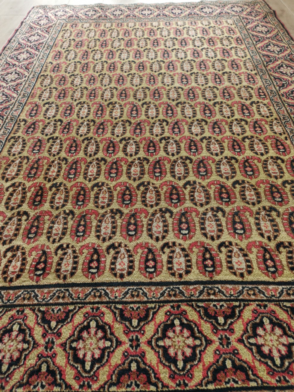 A rectangular hand-knotted Khorassan rug featuring a repeating red boteh pattern on a light yellow field, bordered by a dark floral rosette frame. View IV