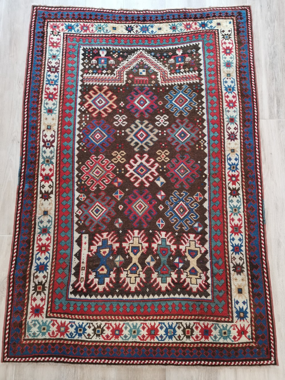An antique hand-knotted Karabagh prayer rug featuring a dark brown central field with a pointed mihrab arch, geometric diamond motifs, and multi-coloured borders.