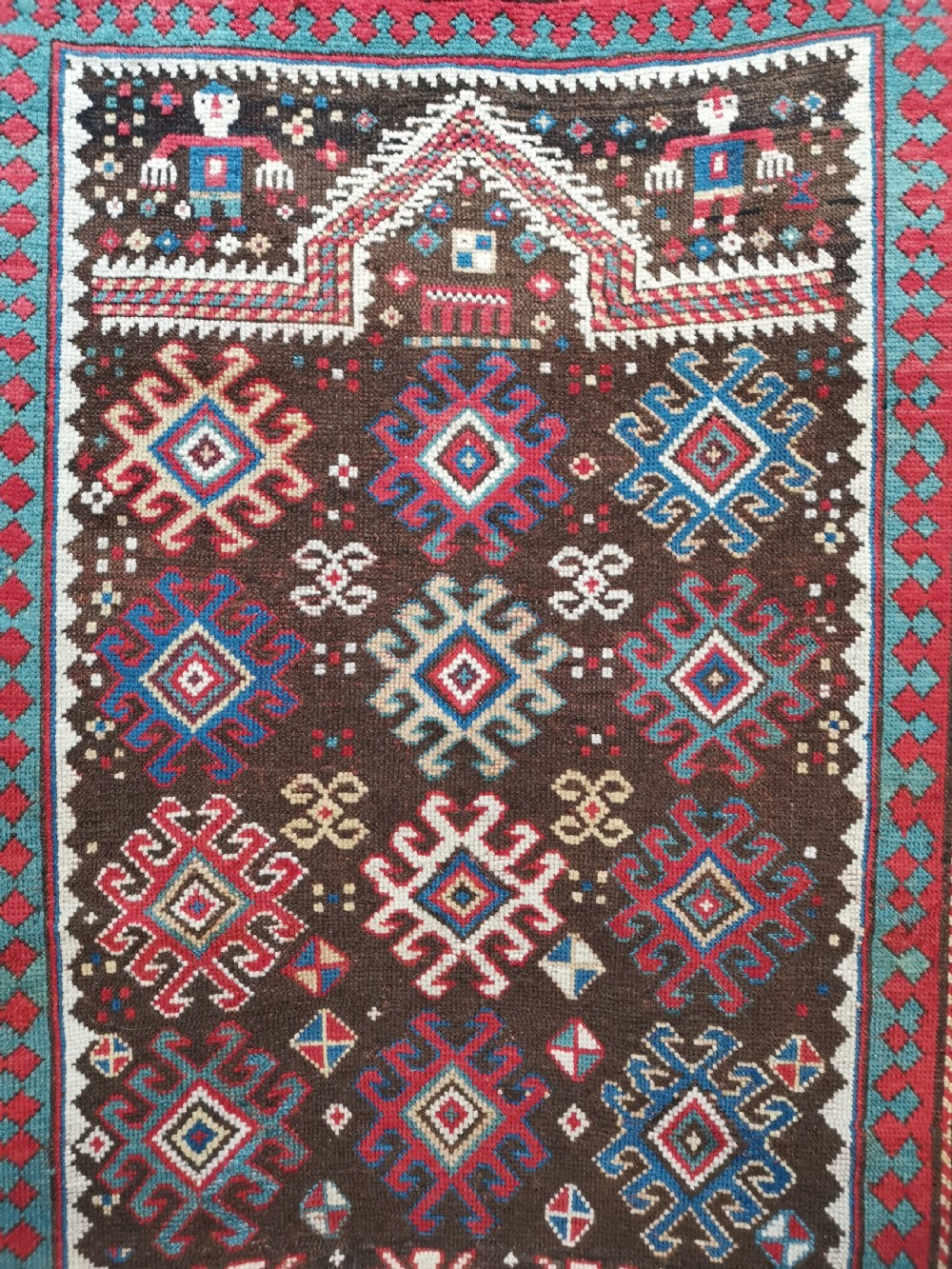 An antique hand-knotted Karabagh prayer rug featuring a dark brown central field with a pointed mihrab arch, geometric diamond motifs, and multi-coloured borders. View II