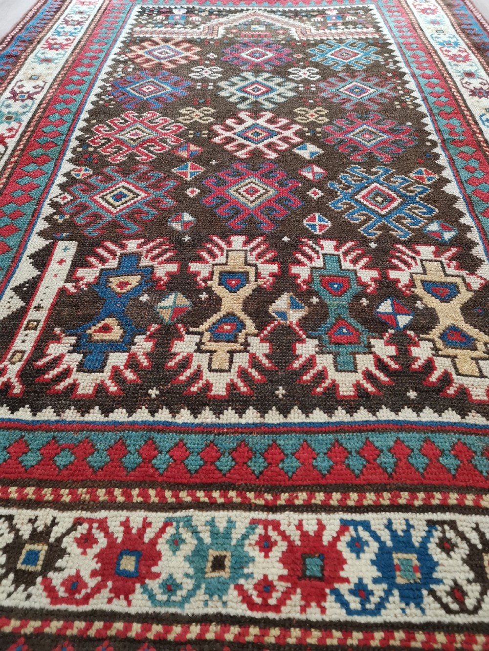 An antique hand-knotted Karabagh prayer rug featuring a dark brown central field with a pointed mihrab arch, geometric diamond motifs, and multi-coloured borders. View VII