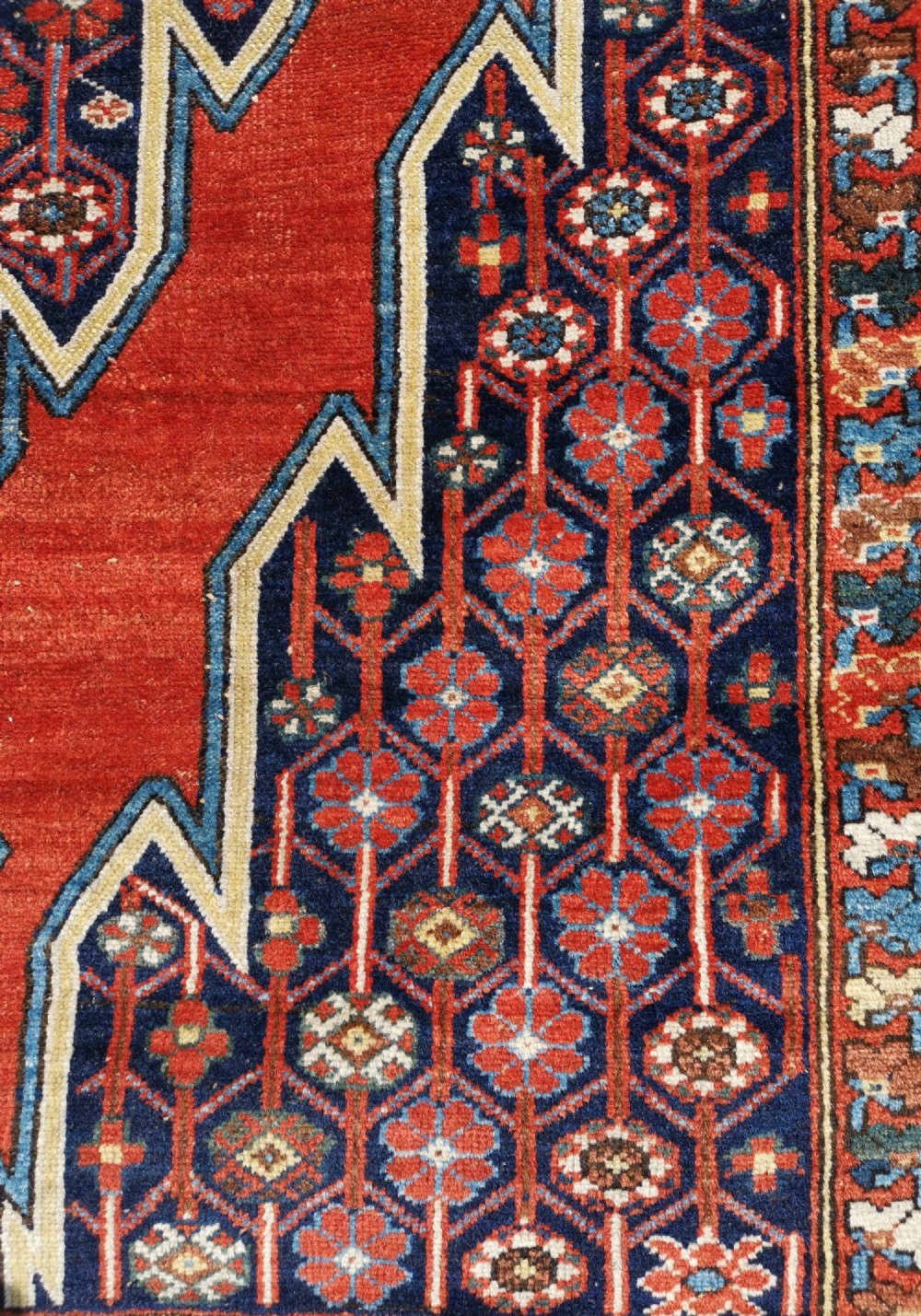 An antique Persian Mazlaghan wool rug featuring a central stepped navy and cream diamond medallion on a terracotta red field with geometric borders. View II