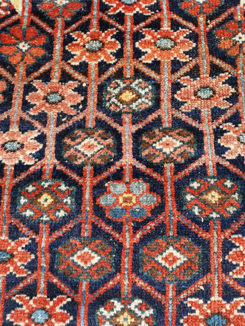 An antique Persian Mazlaghan wool rug featuring a central stepped navy and cream diamond medallion on a terracotta red field with geometric borders. View V