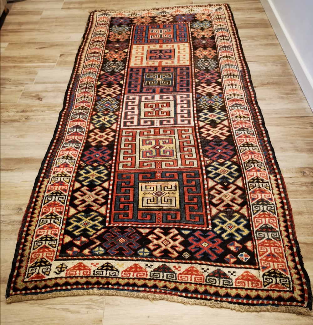 An antique Caucasian Gendje hand-knotted wool runner rug featuring geometric medallions, latch-hook motifs, and a multi-coloured palette of red, blue, yellow, and cream on a dark field.