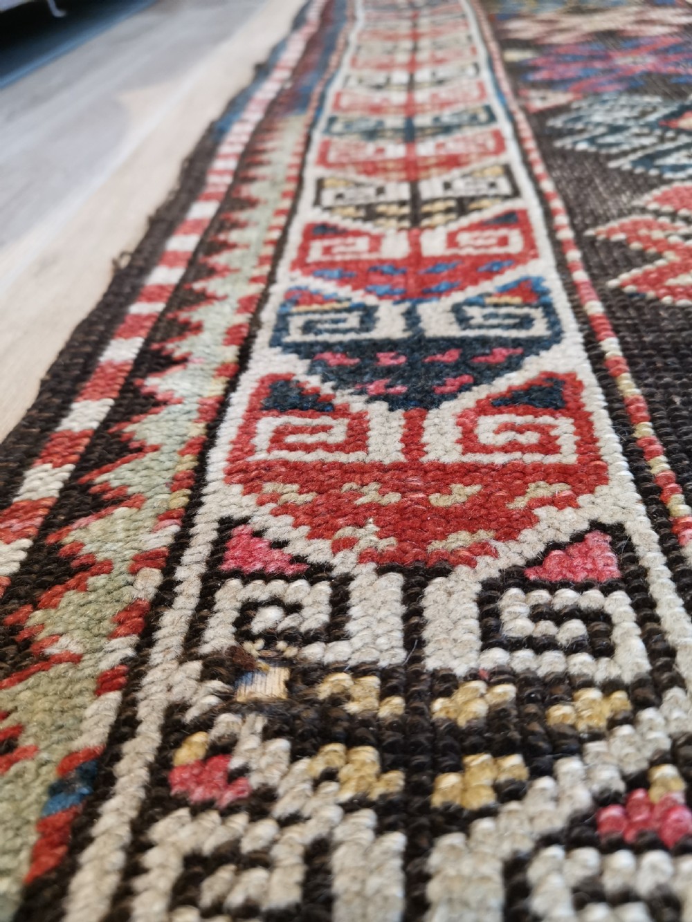 An antique Caucasian Gendje hand-knotted wool runner rug featuring geometric medallions, latch-hook motifs, and a multi-coloured palette of red, blue, yellow, and cream on a dark field. View II