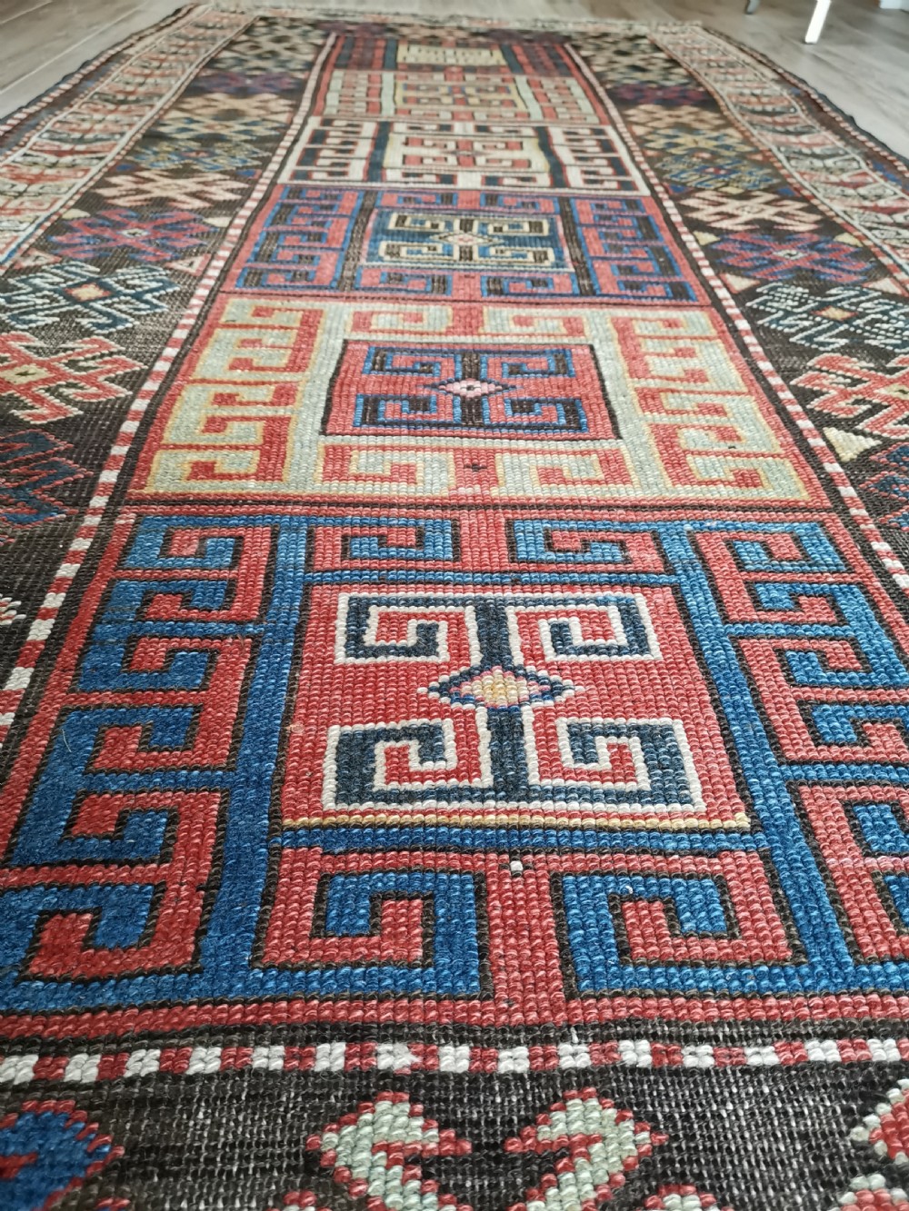 An antique Caucasian Gendje hand-knotted wool runner rug featuring geometric medallions, latch-hook motifs, and a multi-coloured palette of red, blue, yellow, and cream on a dark field. View III