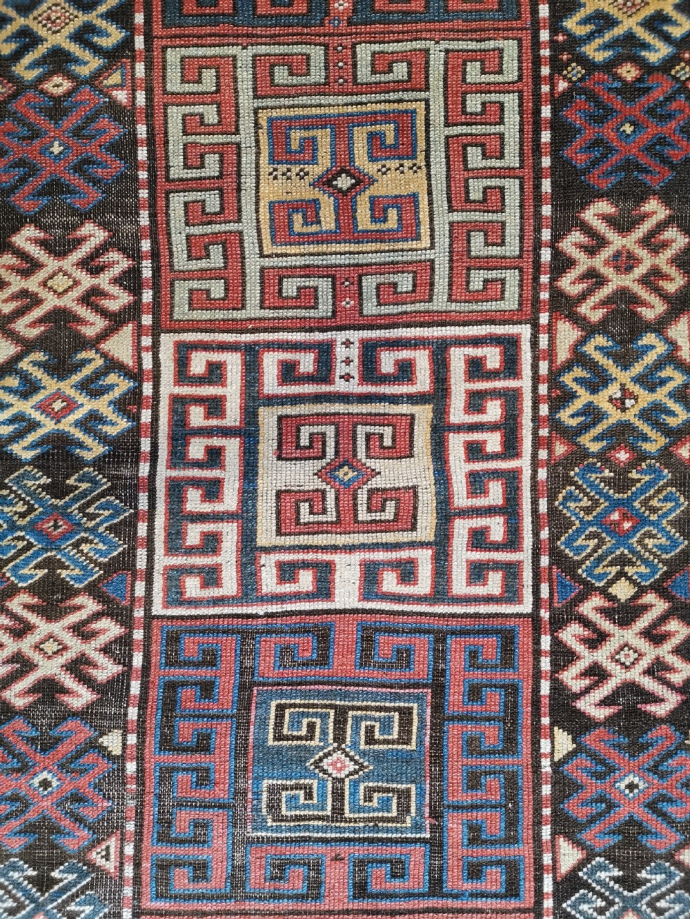 An antique Caucasian Gendje hand-knotted wool runner rug featuring geometric medallions, latch-hook motifs, and a multi-coloured palette of red, blue, yellow, and cream on a dark field. View VI