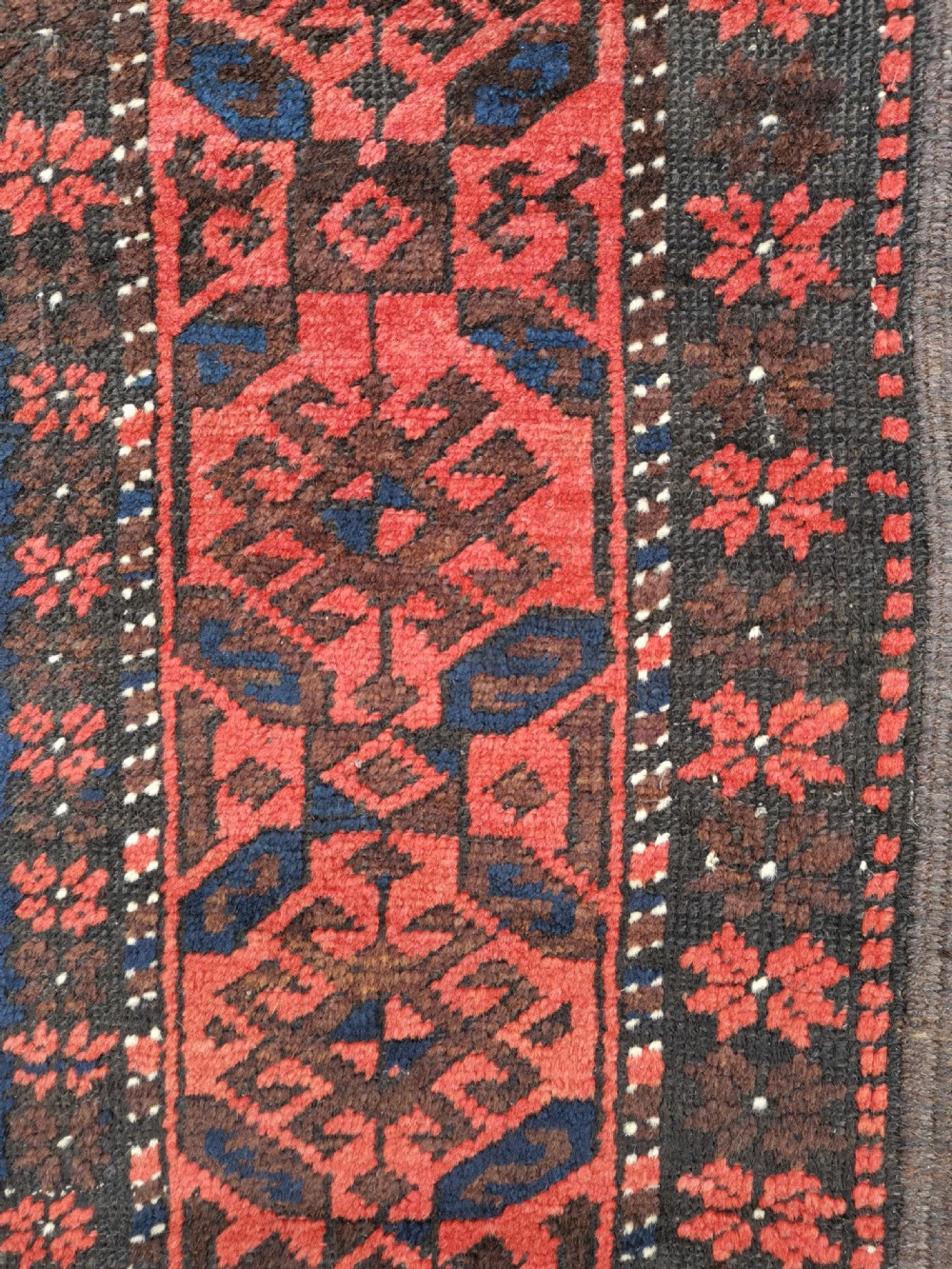 A hand-knotted Belouch wool rug featuring dark indigo blue and deep red geometric motifs framed by a decorative patterned border and cream fringes. View II