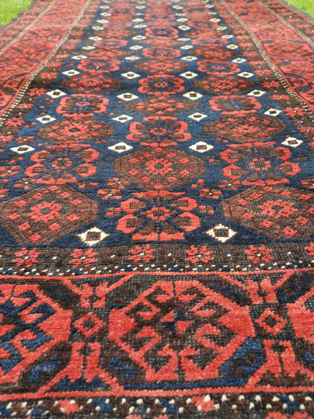 A hand-knotted Belouch wool rug featuring dark indigo blue and deep red geometric motifs framed by a decorative patterned border and cream fringes. View III