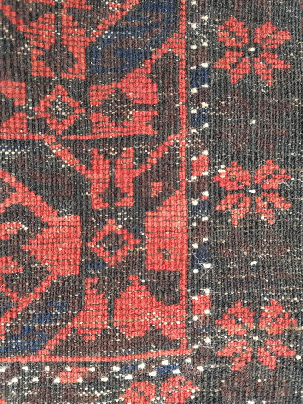 A hand-knotted Belouch wool rug featuring dark indigo blue and deep red geometric motifs framed by a decorative patterned border and cream fringes. View IV