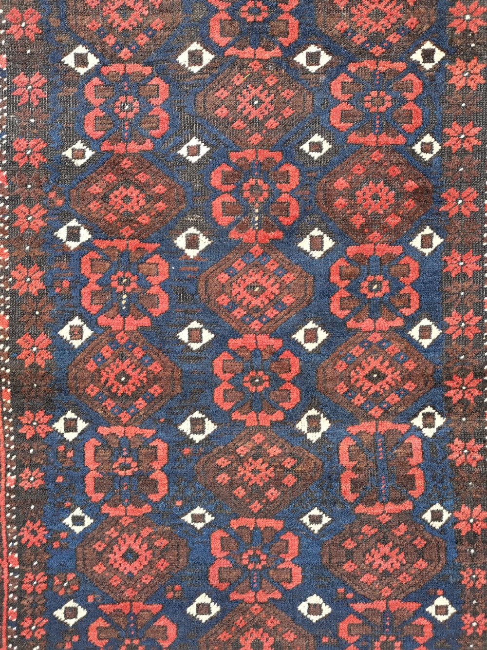 A hand-knotted Belouch wool rug featuring dark indigo blue and deep red geometric motifs framed by a decorative patterned border and cream fringes. View V