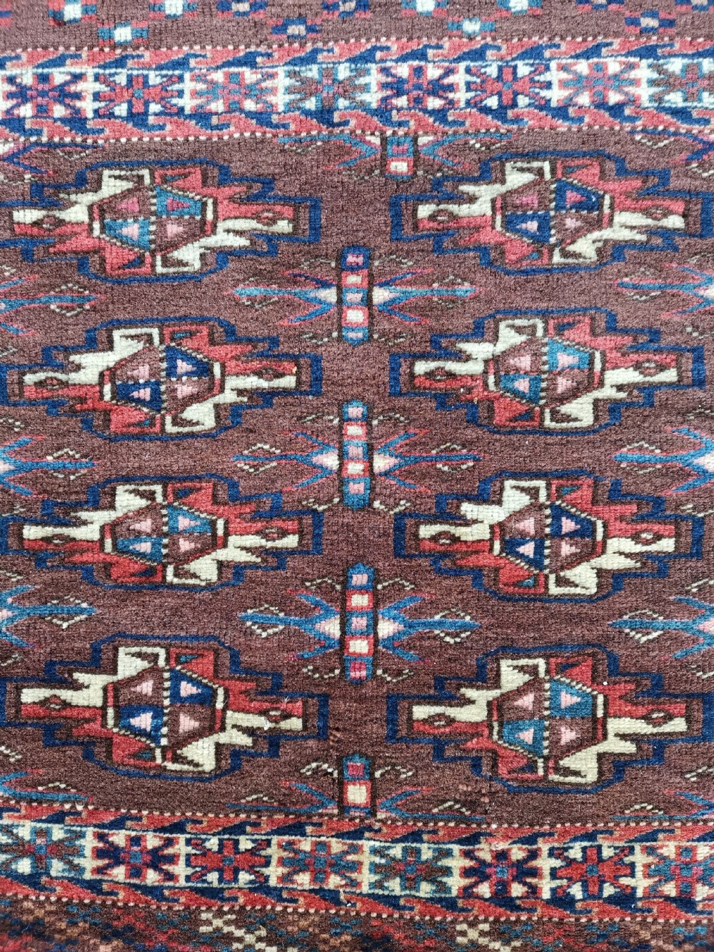 A rectangular hand-knotted wool Yomut chuval featuring rows of geometric guls on a reddish brown field above a patterned lower elem panel. View II