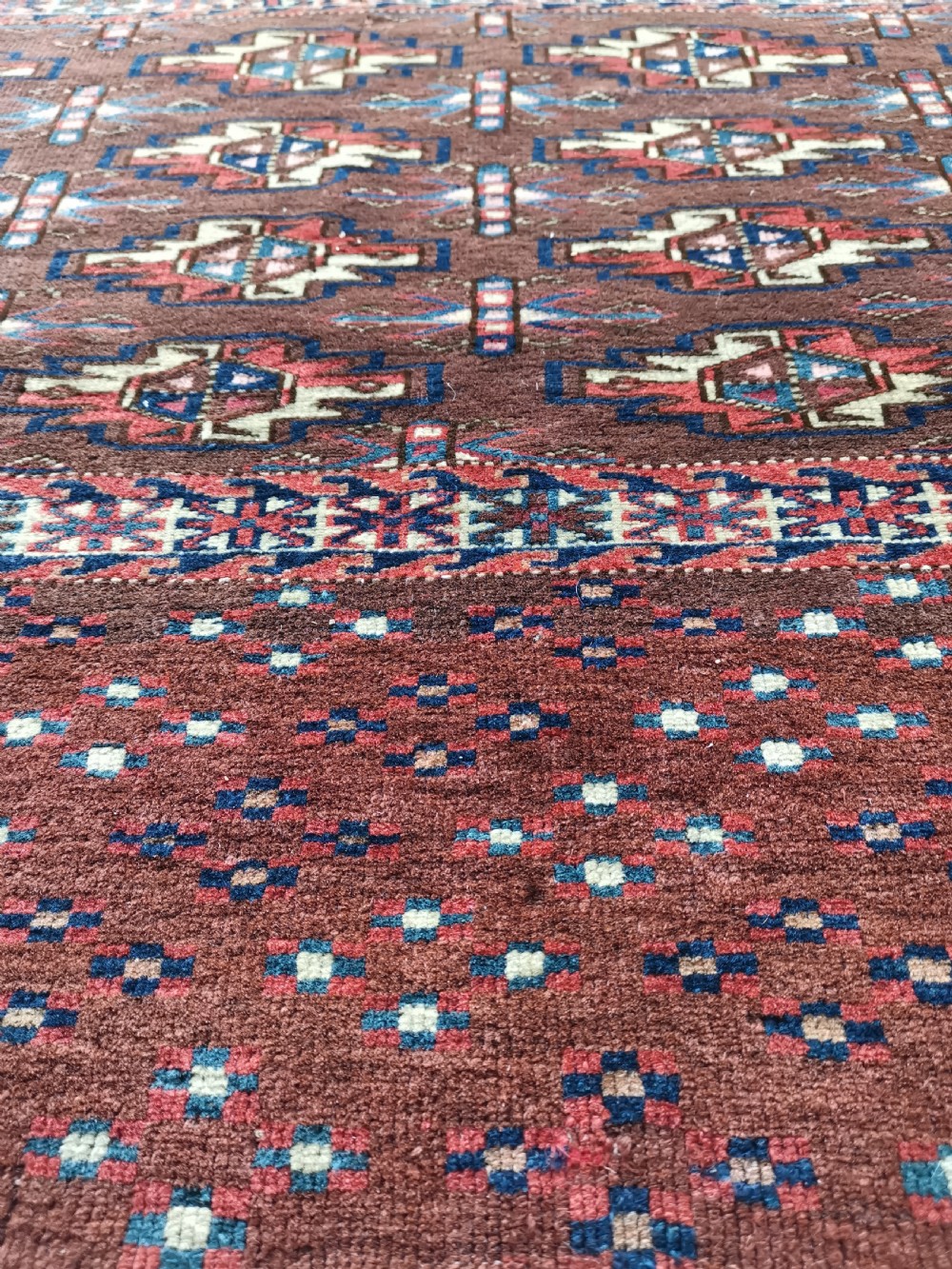 A rectangular hand-knotted wool Yomut chuval featuring rows of geometric guls on a reddish brown field above a patterned lower elem panel. View V