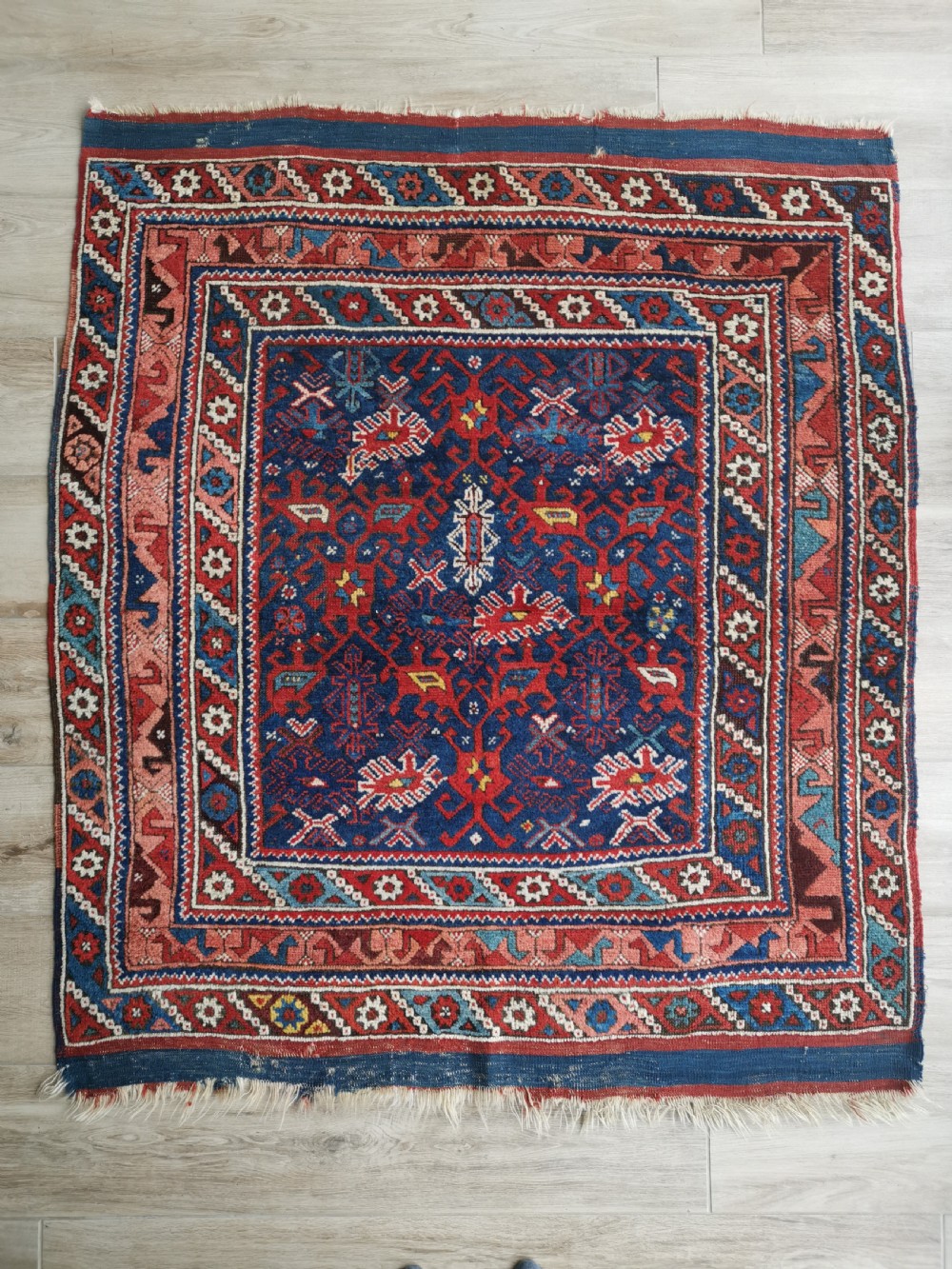 A hand-knotted Anatolian wool rug featuring a deep navy blue central field filled with geometric tribal motifs surrounded by layered madder red and blue borders.