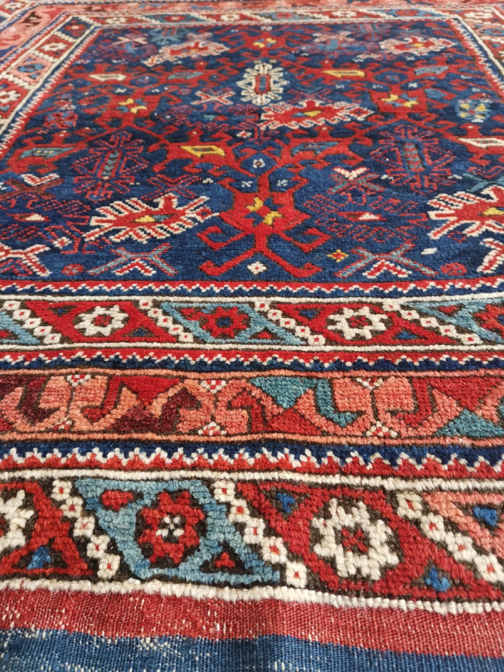 A hand-knotted Anatolian wool rug featuring a deep navy blue central field filled with geometric tribal motifs surrounded by layered madder red and blue borders. View IV