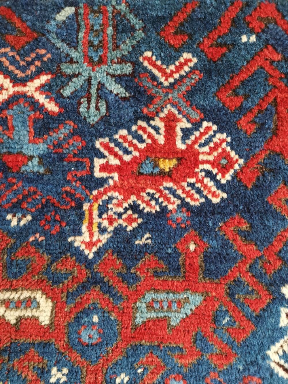 A hand-knotted Anatolian wool rug featuring a deep navy blue central field filled with geometric tribal motifs surrounded by layered madder red and blue borders. View V