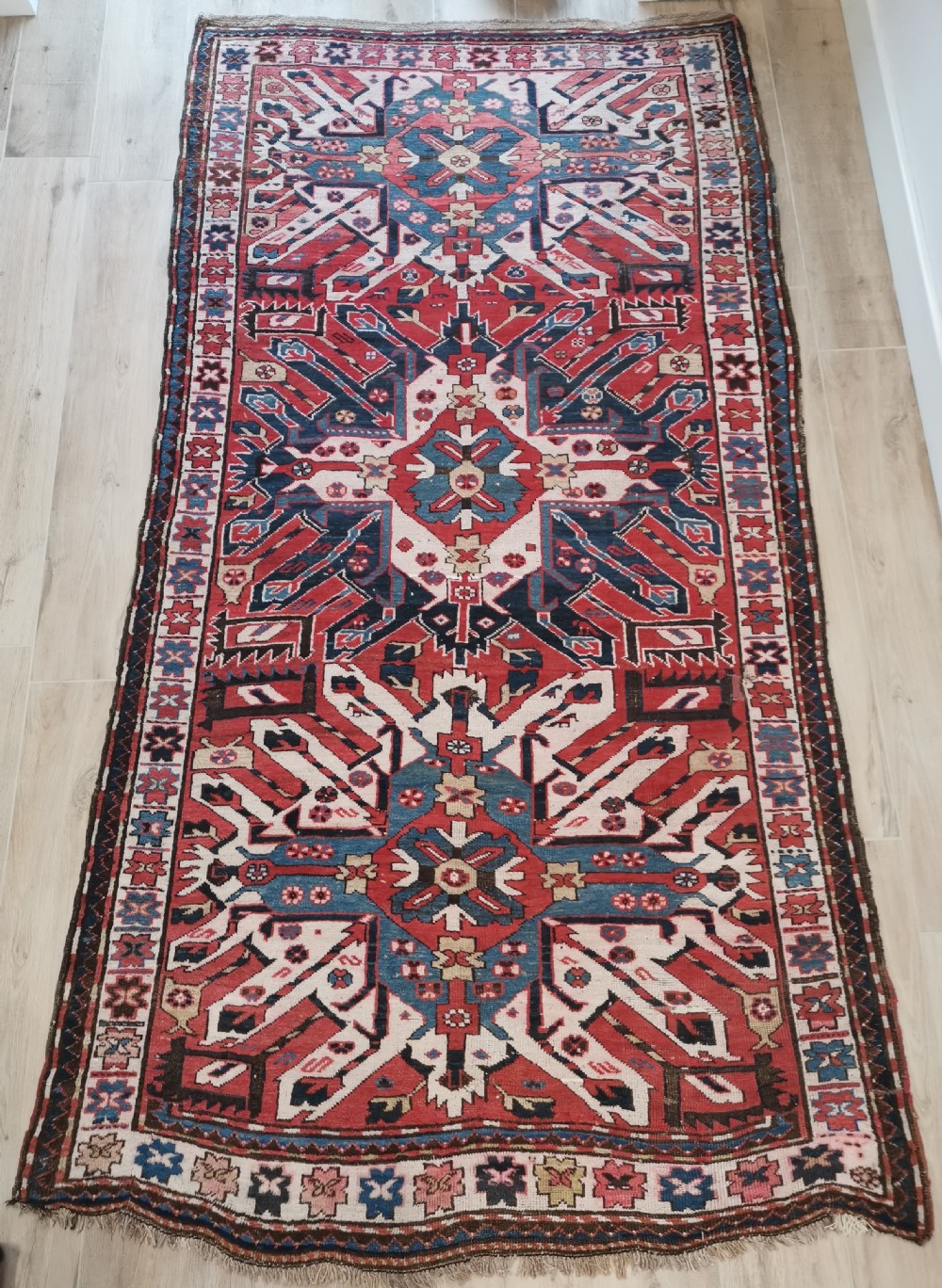 A rectangular hand-knotted Caucasian Chelaberd rug featuring prominent sunburst medallions in red, navy blue, and ivory with geometric borders.