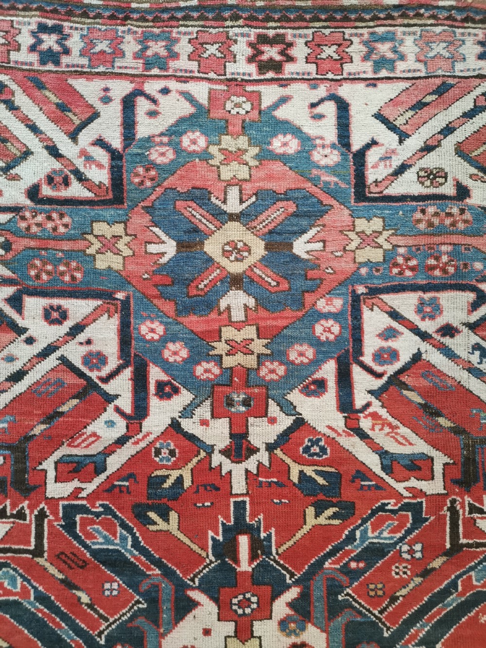 A rectangular hand-knotted Caucasian Chelaberd rug featuring prominent sunburst medallions in red, navy blue, and ivory with geometric borders. View III
