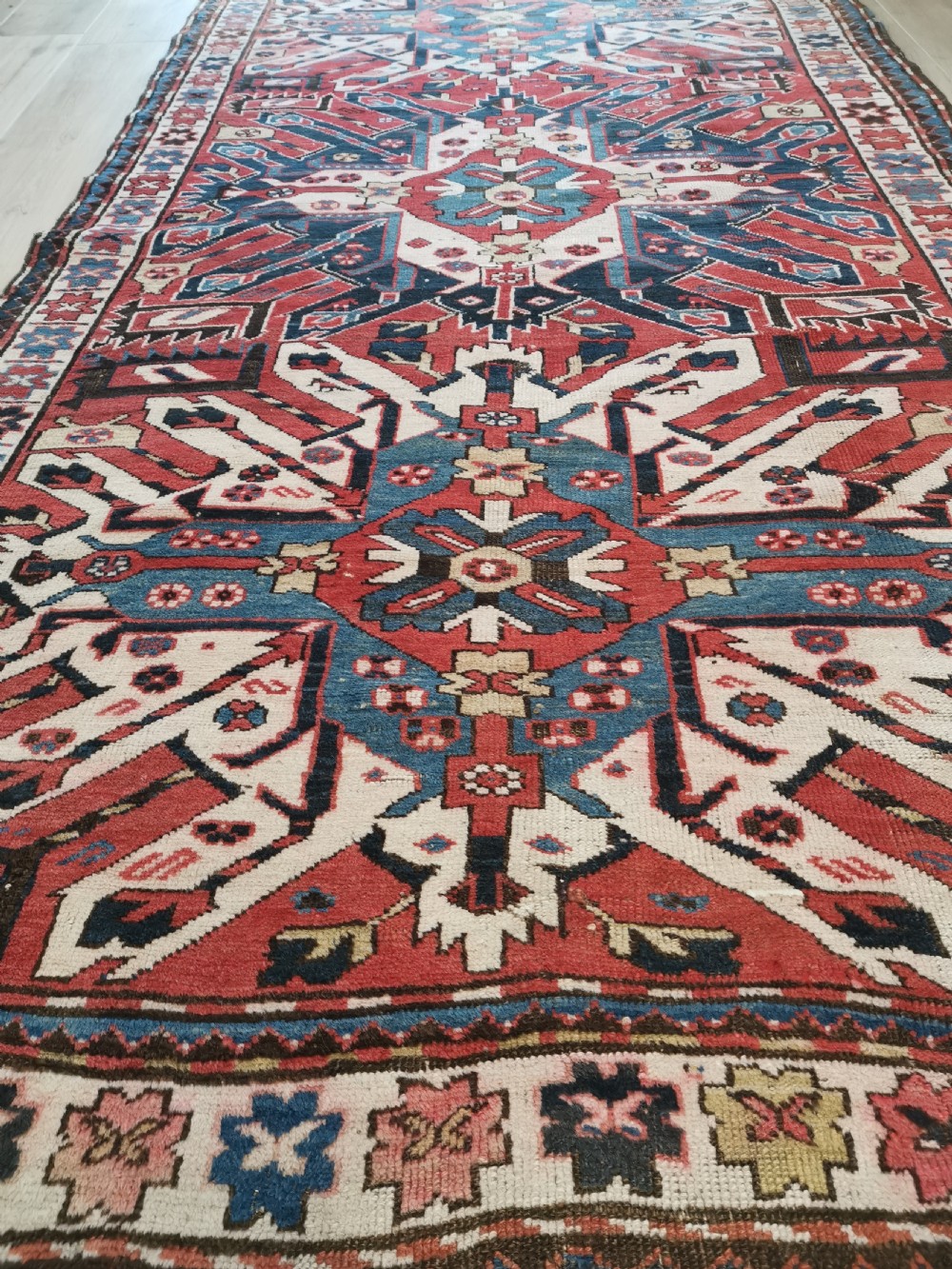 A rectangular hand-knotted Caucasian Chelaberd rug featuring prominent sunburst medallions in red, navy blue, and ivory with geometric borders. View IV