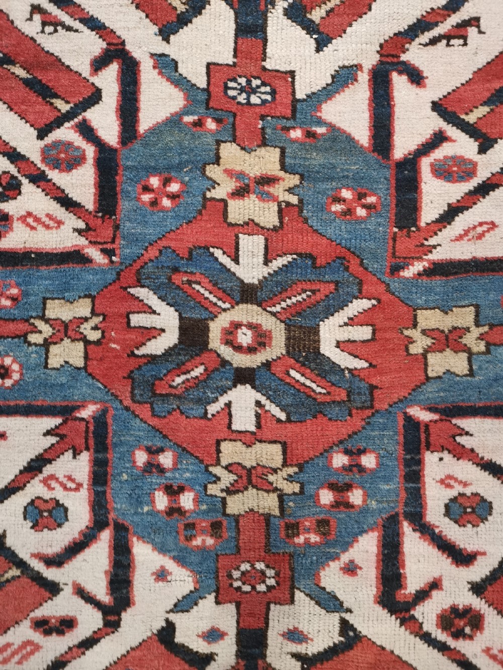 A rectangular hand-knotted Caucasian Chelaberd rug featuring prominent sunburst medallions in red, navy blue, and ivory with geometric borders. View V