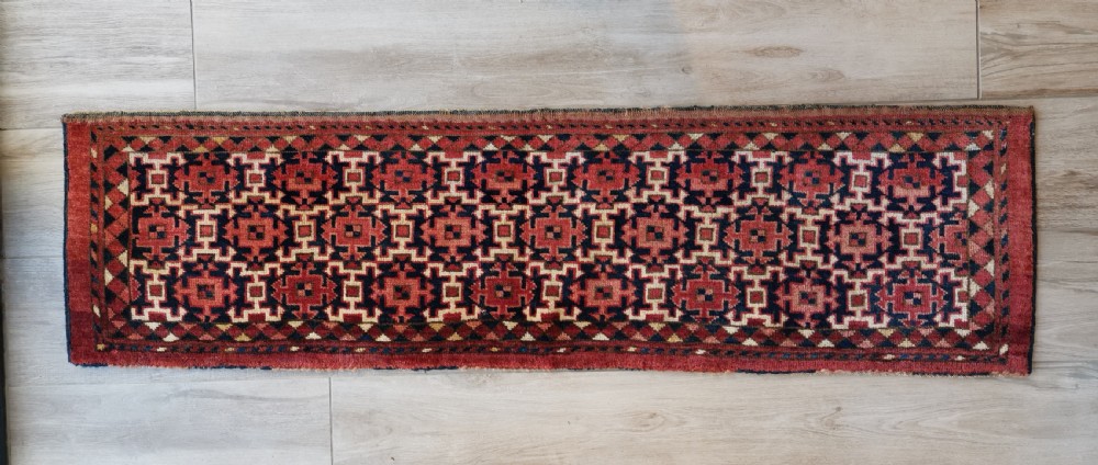 A long, rectangular hand-knotted Ersari torba textile displaying repeating geometric red, navy blue, and cream motifs framed by a narrow patterned border.