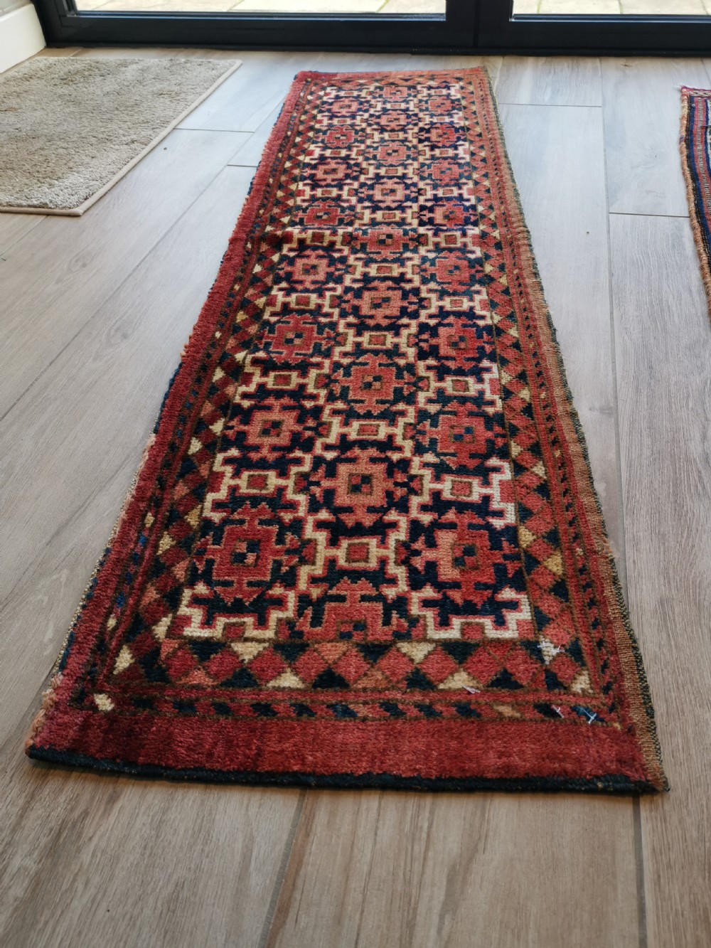 A long, rectangular hand-knotted Ersari torba textile displaying repeating geometric red, navy blue, and cream motifs framed by a narrow patterned border. View III