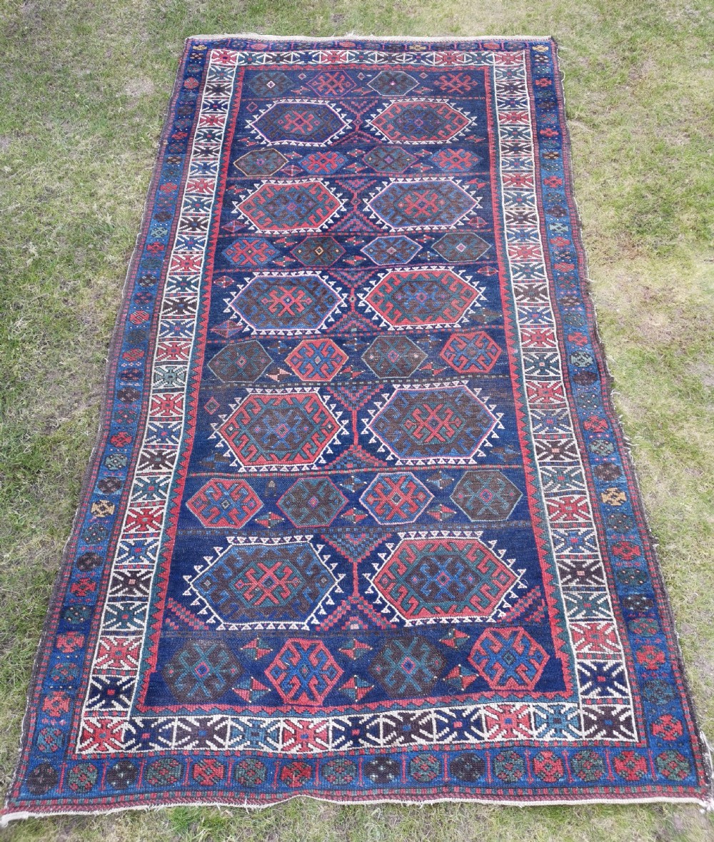 A hand-knotted wool rug with repeating hexagonal geometric medallions in red and turquoise set against a navy blue field.