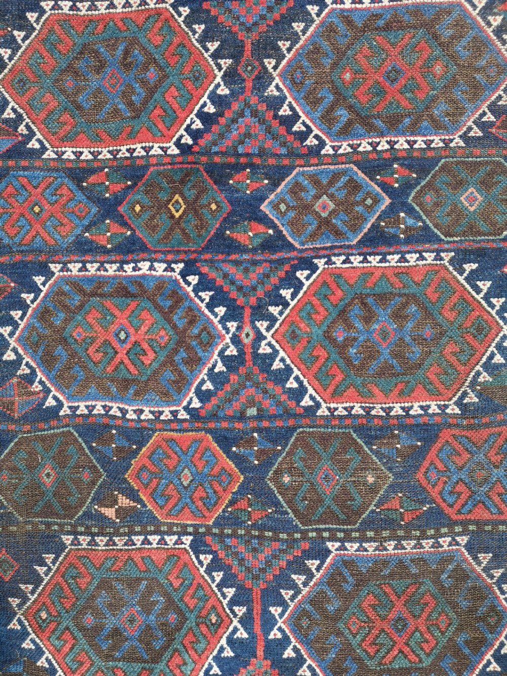 A hand-knotted wool rug with repeating hexagonal geometric medallions in red and turquoise set against a navy blue field. View II
