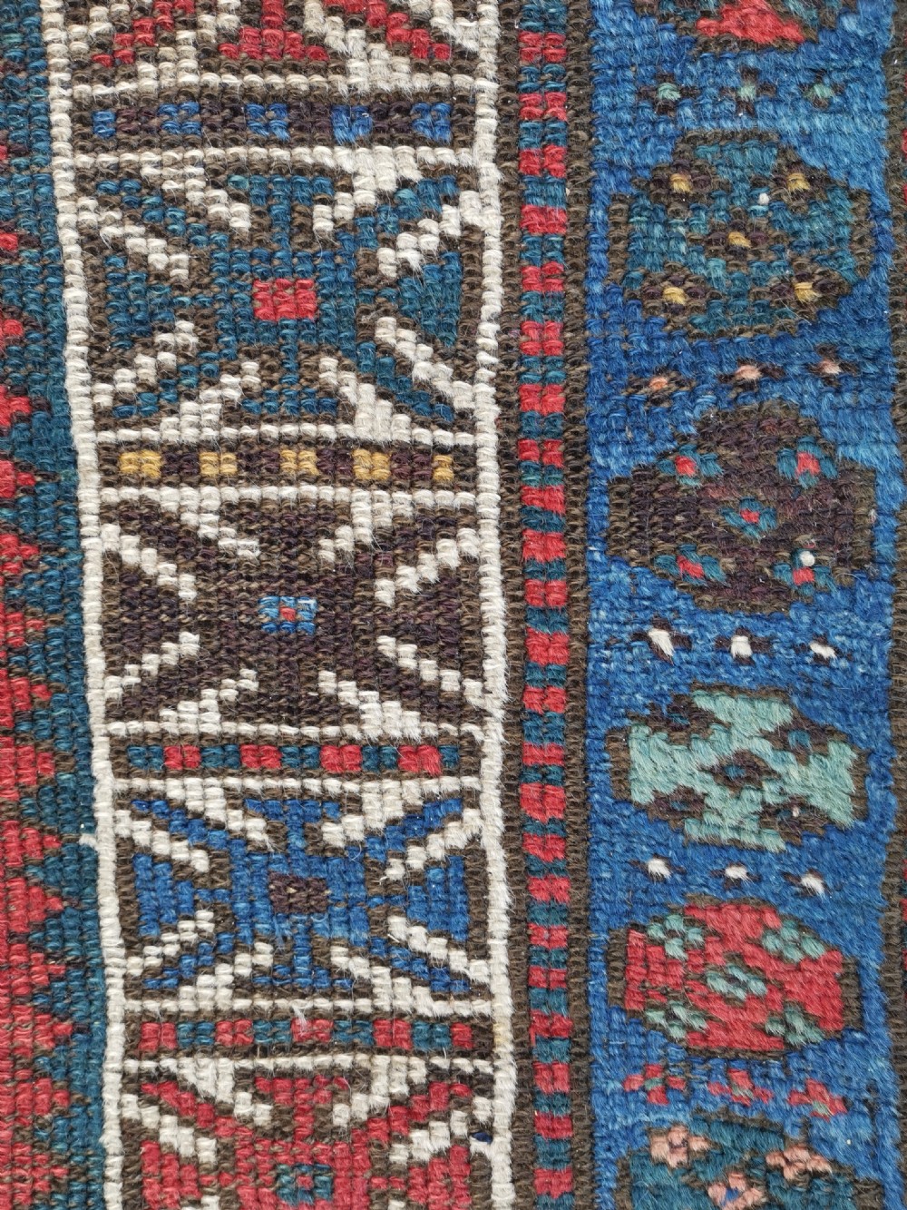 A hand-knotted wool rug with repeating hexagonal geometric medallions in red and turquoise set against a navy blue field. View III