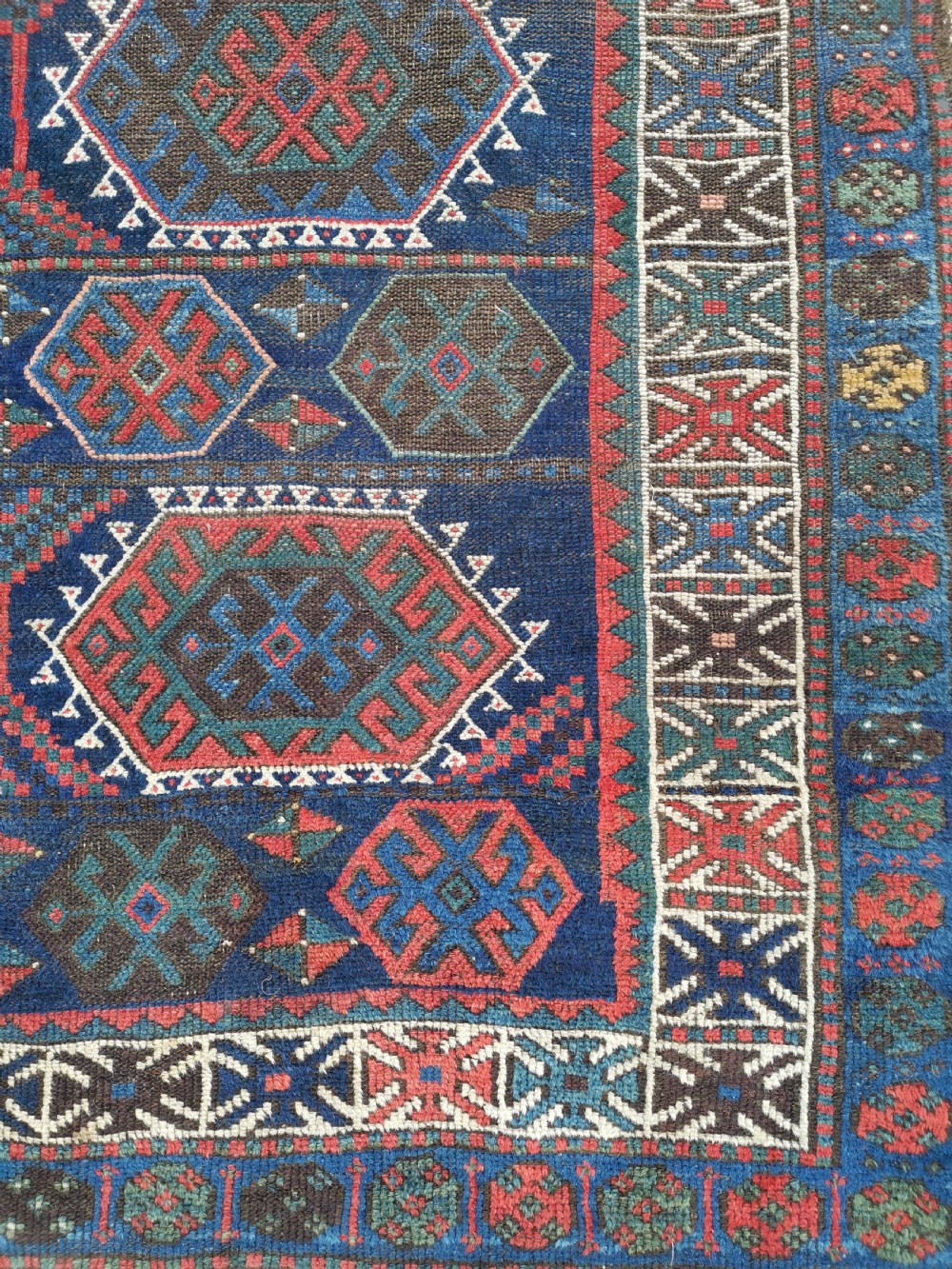 A hand-knotted wool rug with repeating hexagonal geometric medallions in red and turquoise set against a navy blue field. View IV