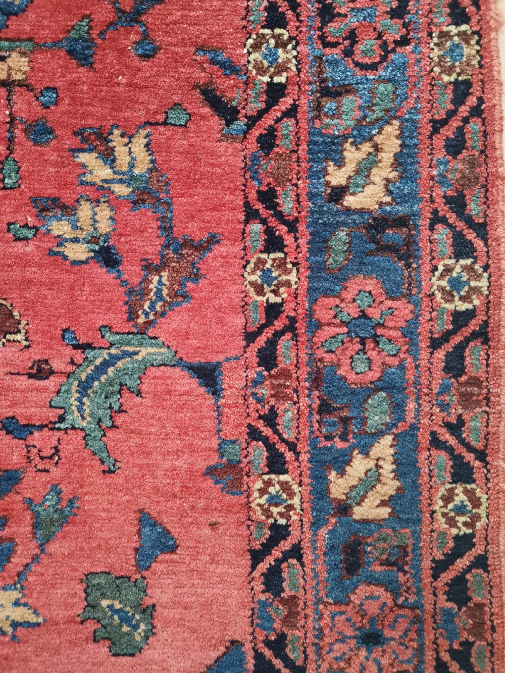 A hand-knotted antique Persian Hamadan rug featuring a central navy blue medallion on a red field framed by patterned borders. View V