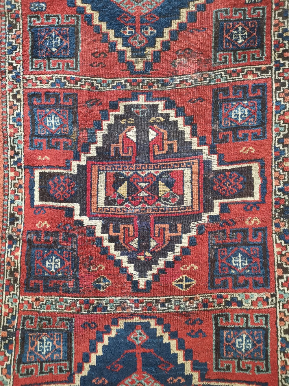 An antique East Anatolian Kurdish wool rug featuring a red ground with three large geometric medallions in indigo blue, framed by intricate tribal borders. View II