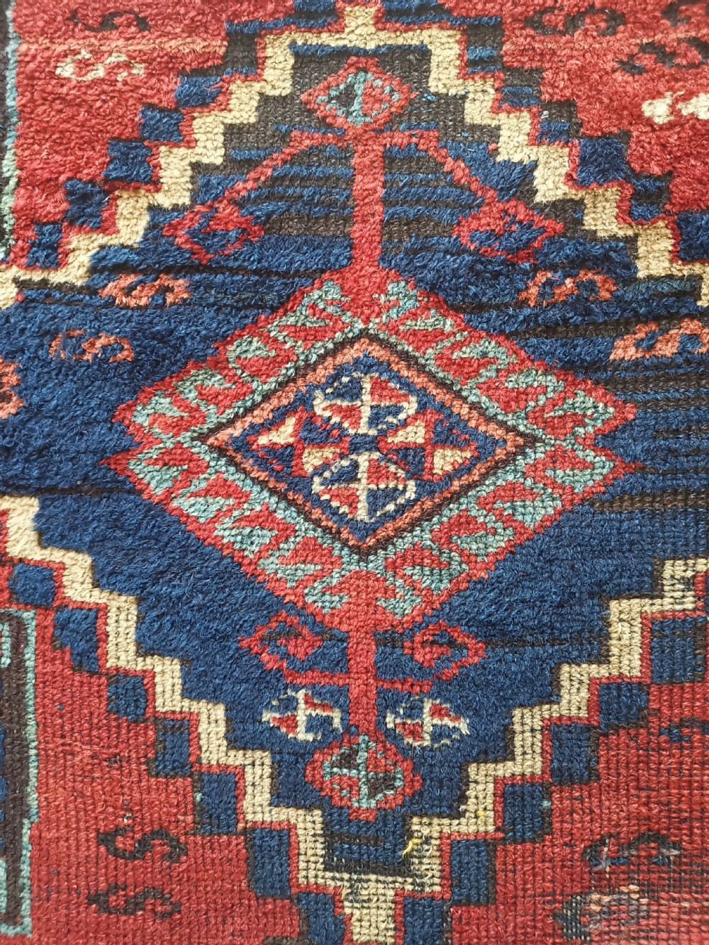An antique East Anatolian Kurdish wool rug featuring a red ground with three large geometric medallions in indigo blue, framed by intricate tribal borders. View III
